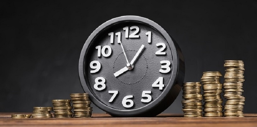 round-clock-between-the-increasing-coins-on-wooden-desk-against-black-backdrop